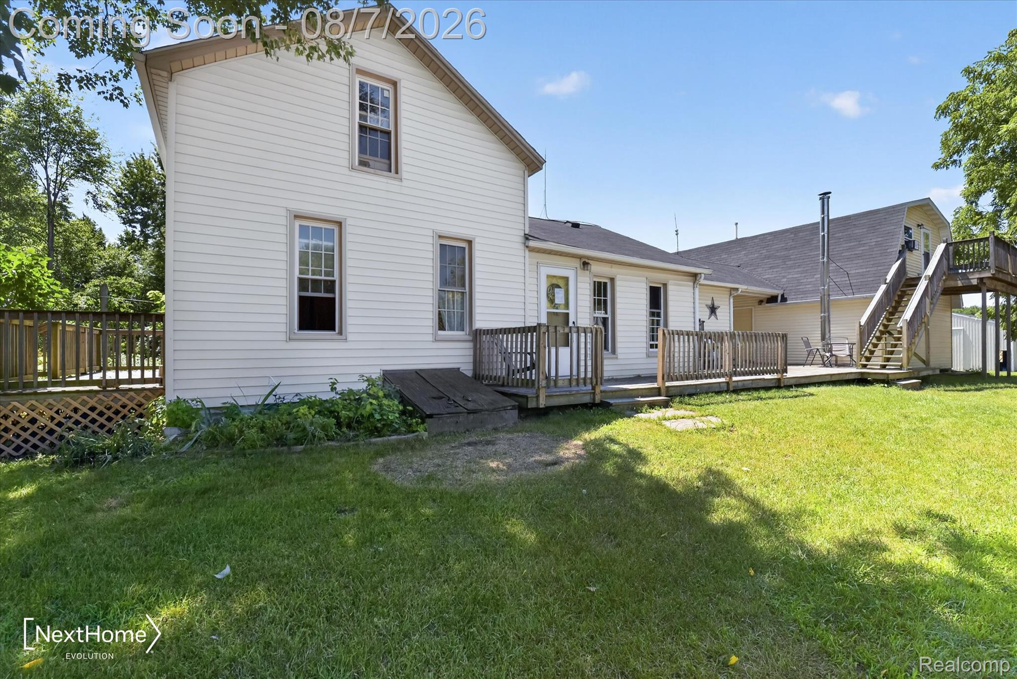 23740 Carleton West Road Belleville, MI 48111 - Photo 5 of 58 Expansive rear yard featuring a large wooden deck, partial lattice skirting, and a second-story exterior staircase