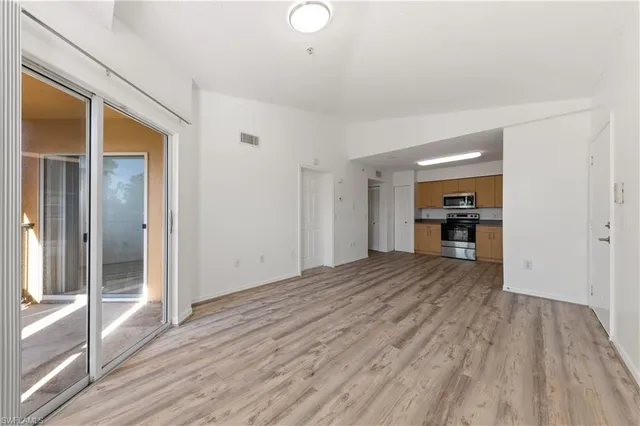 a view of empty room with wooden floor and kitchen view