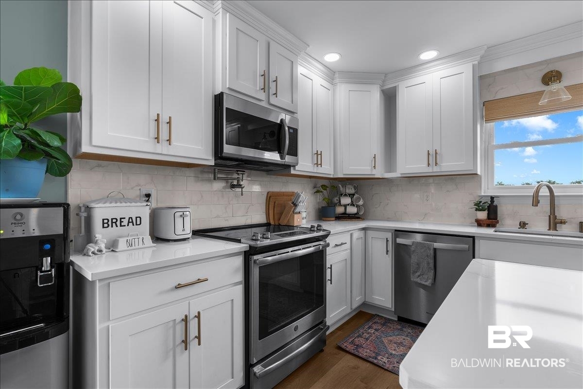 8952 Sherman Road Foley, AL 36535 - Photo 18 of 41 Modern kitchen featuring white shaker cabinetry with gold-finish hardware, stainless steel appliances, white countertops, and a subway tile backsplash