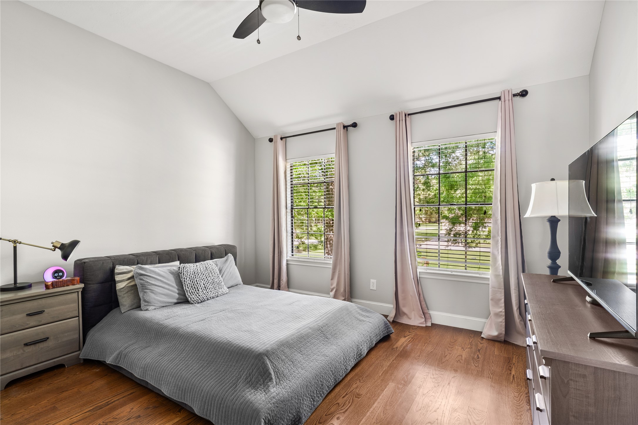 36 Wind River Drive Conroe, TX 77384 - Photo 35 of 45 This bedroom features two large windows with soft drapes, allowing plenty of natural light, and a ceiling fan for comfort. The room has hardwood floors and neutral walls, creating a welcoming atmosphere.