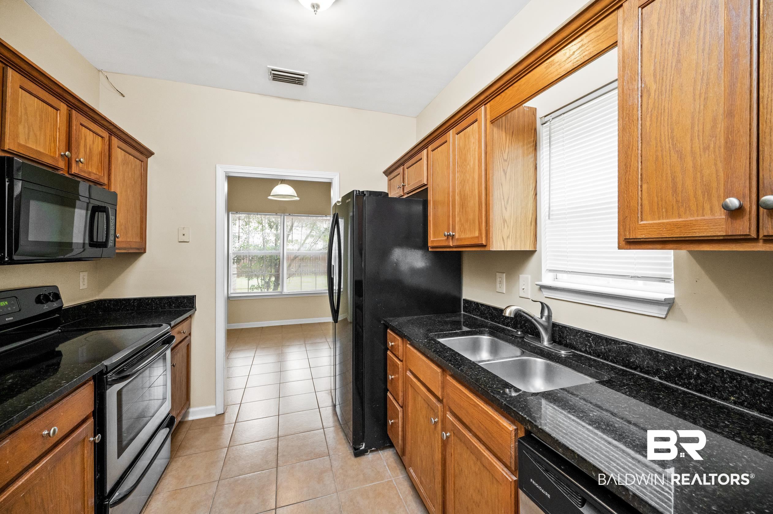 1333 Dominoe Trail Foley, AL 36535 - Photo 9 of 32 Kitchen featuring black appliances, light tile patterned floors, dark stone counters, and sink