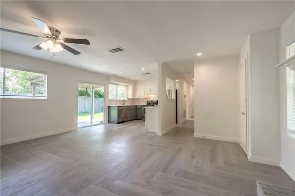 a view of an empty room with wooden floor and a kitchen