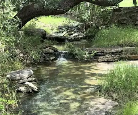 4215 Sunset Cliff Road Burnet, TX 78611 - Photo 11 of 13 A tranquil stream meanders through verdant landscaping, offering a peaceful natural setting.