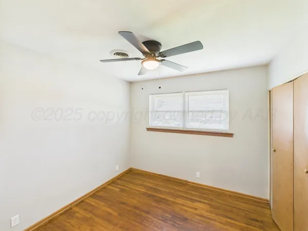 an empty room with wooden floor ceiling fan and windows