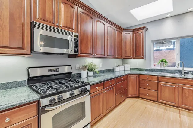 a kitchen with stainless steel appliances granite countertop a stove a sink dishwasher a dining table and chairs with wooden floor