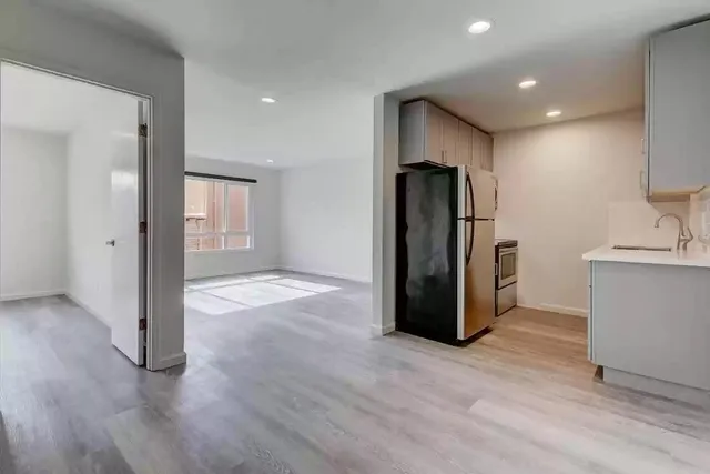 a view of a refrigerator in kitchen and an empty room with wooden floor and a window