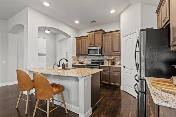 a kitchen with stainless steel appliances granite countertop a refrigerator a sink dishwasher a stove with wooden cabinets and floor