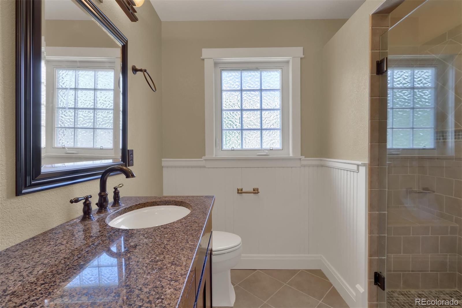3045 Hay Creek Road Colorado Springs, CO 80921 - Photo 23 of 40 a bathroom with a granite countertop sink toilet a mirror and shower