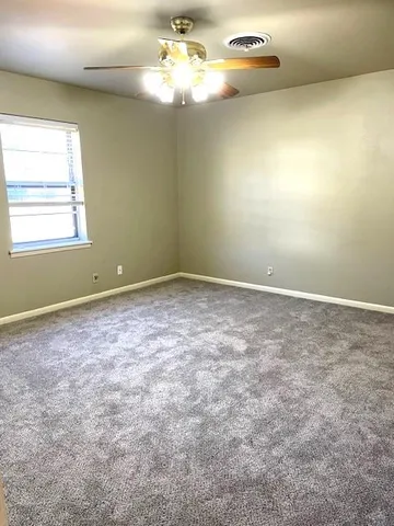 an empty room with chandelier fan and windows