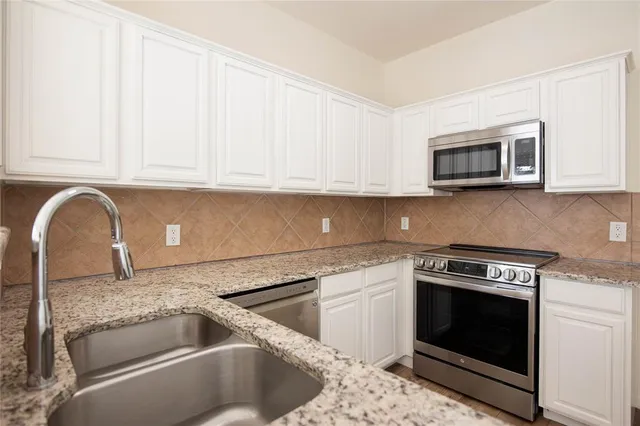 a kitchen with granite countertop white cabinets and stainless steel appliances