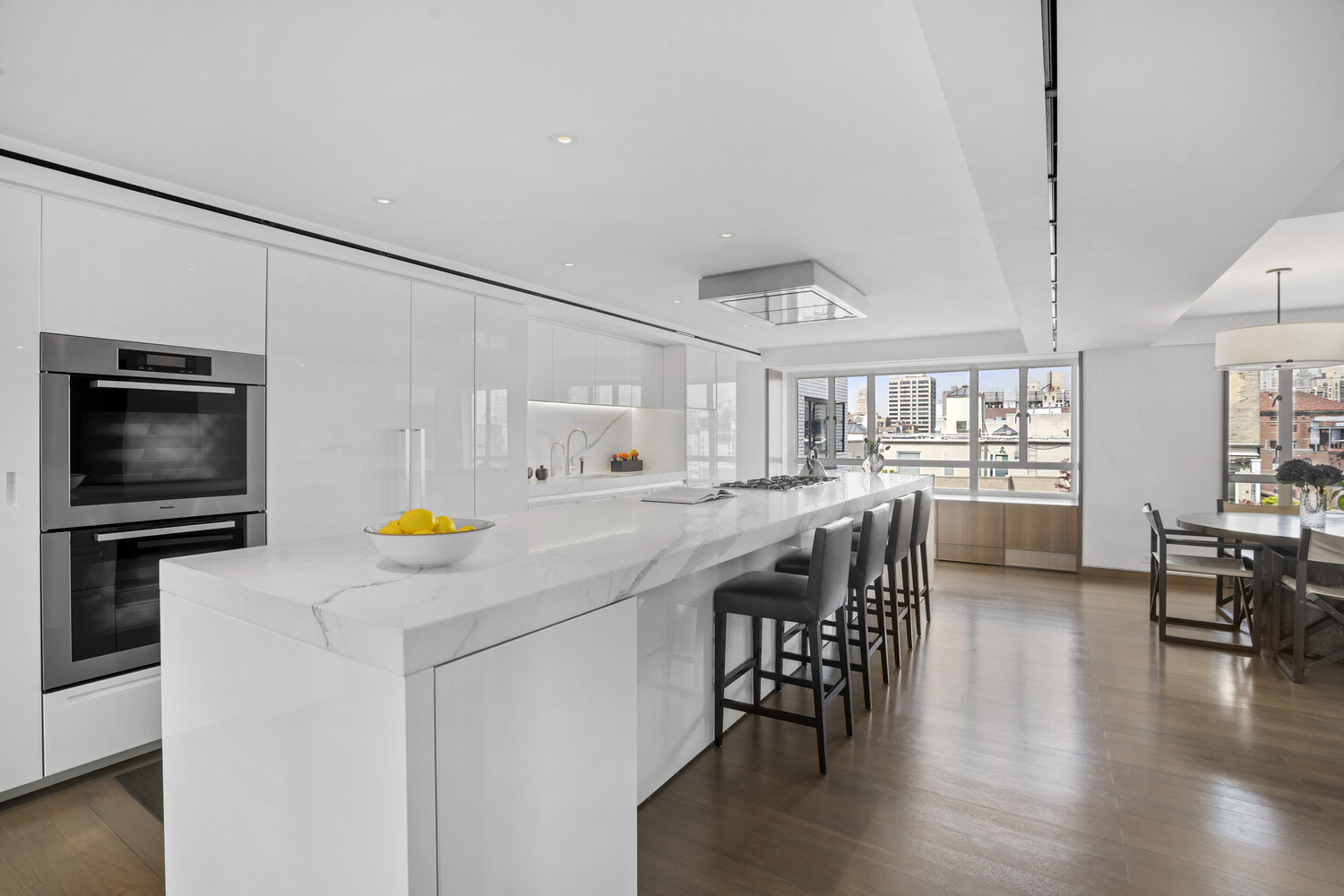 799 Park Avenue, Unit 19BC Manhattan, NY 10021 - Photo 3 of 12 a kitchen with stainless steel appliances a stove a sink a microwave a dining table and chairs with wooden floor