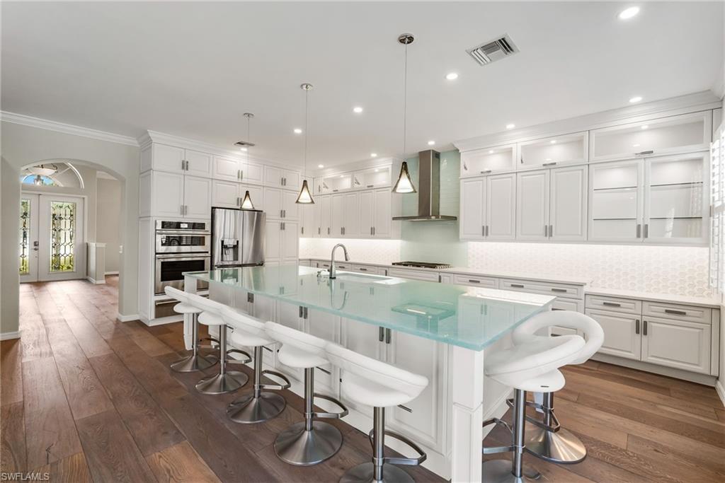 5801 Lago Villaggio Way Naples, FL 34104 - Photo 3 of 23 Kitchen featuring white cabinets, a kitchen breakfast bar, arched walkways, tasteful backsplash, and an island with sink