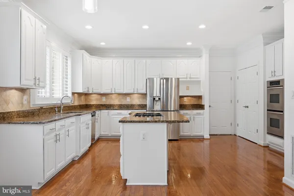 a kitchen with stainless steel appliances granite countertop a refrigerator a stove top oven a sink and dishwasher with wooden floor