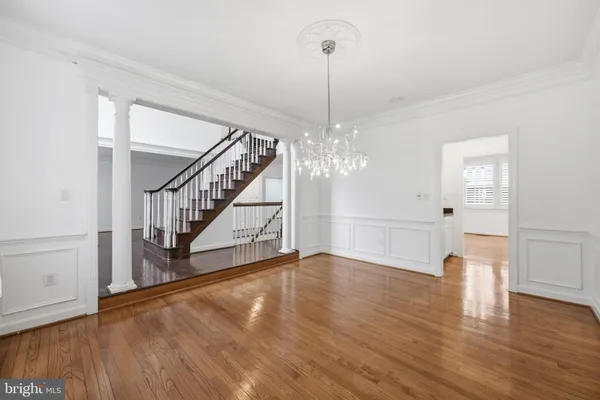 a view of an empty room with wooden floor staircase and a chandelier