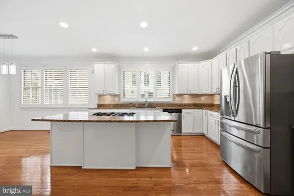 a kitchen with stainless steel appliances granite countertop a stove a sink dishwasher a refrigerator and white cabinets with wooden floor