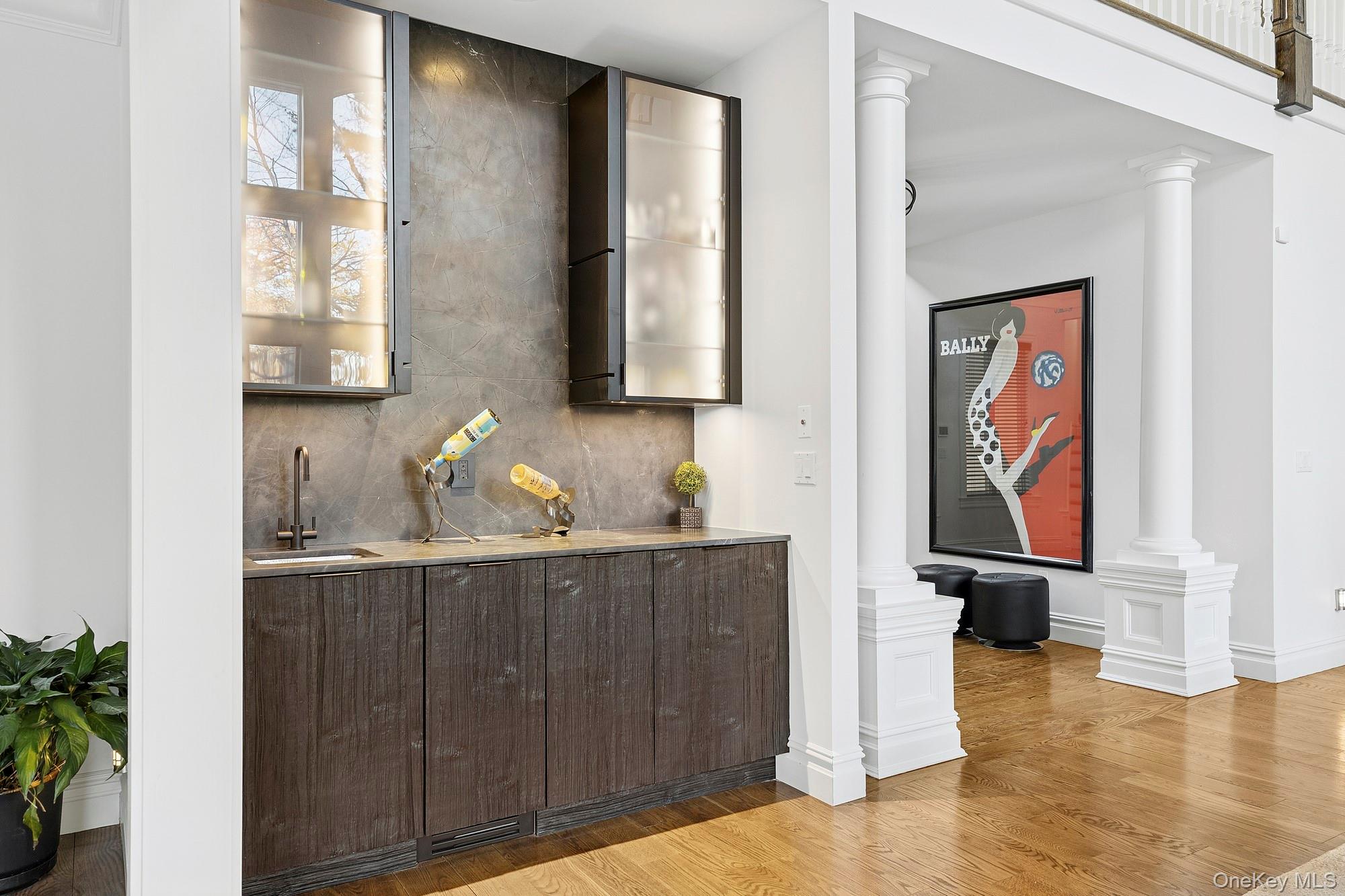 144 Round Swamp Road West Hills, NY 11743 - Photo 15 of 39 Indoor wet bar featuring glass insert cabinets, light wood-type flooring, tasteful backsplash, modern cabinets, and decorative columns
