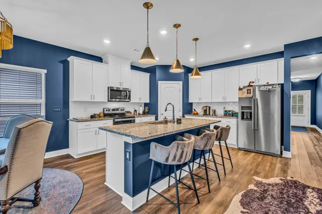 a kitchen with stainless steel appliances granite countertop a sink a stove a refrigerator and island with wooden floor