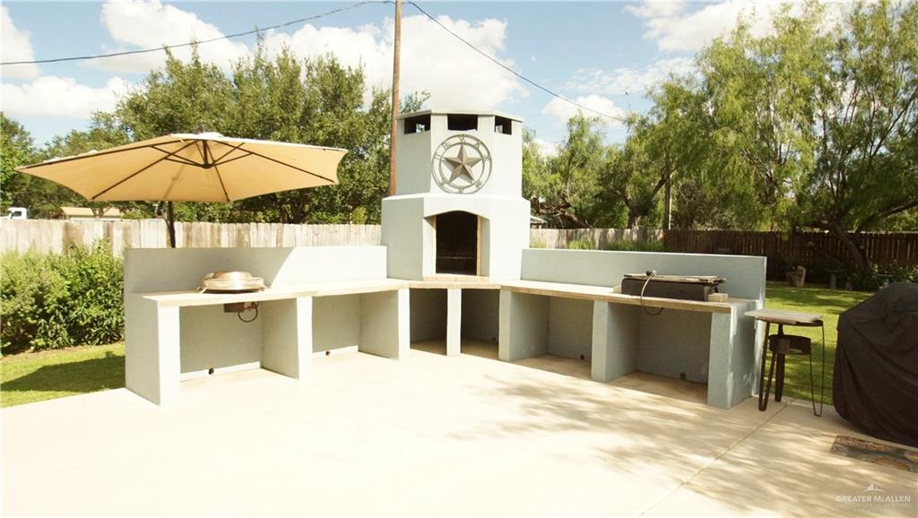 414 Ric Mar Street Edinburg, TX 78541 - Photo 3 of 36 Outdoor kitchen featuring a central fireplace with stone accents, extensive built-in counter space, and a concrete patio