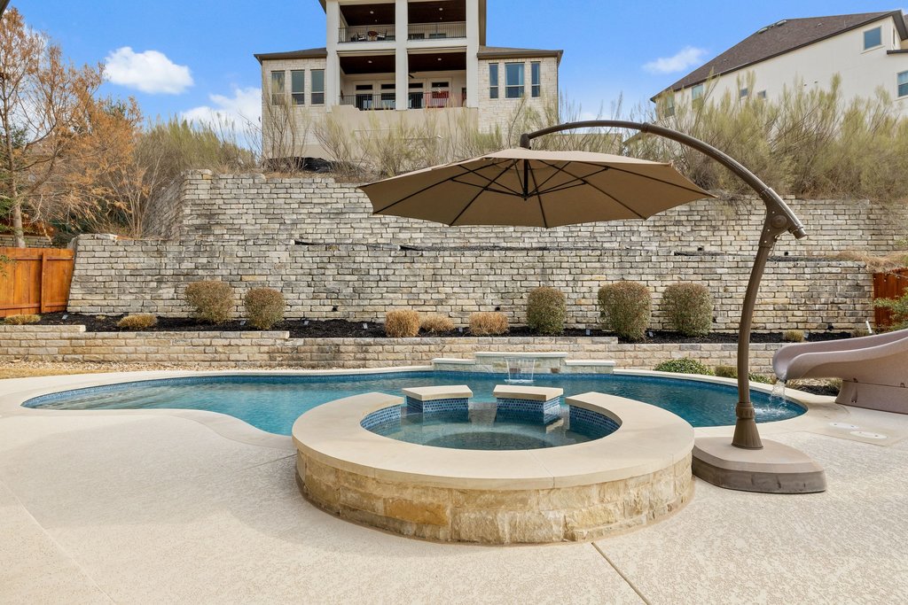 5812 Davenport Divide Road Austin, TX 78738 - Photo 34 of 40 A resort-style backyard anchored by a circular raised spa finished in stone and tile. The umbrella feature adds architectural interest while providing shade, and the retaining wall backdrop gives dimension and privacy.