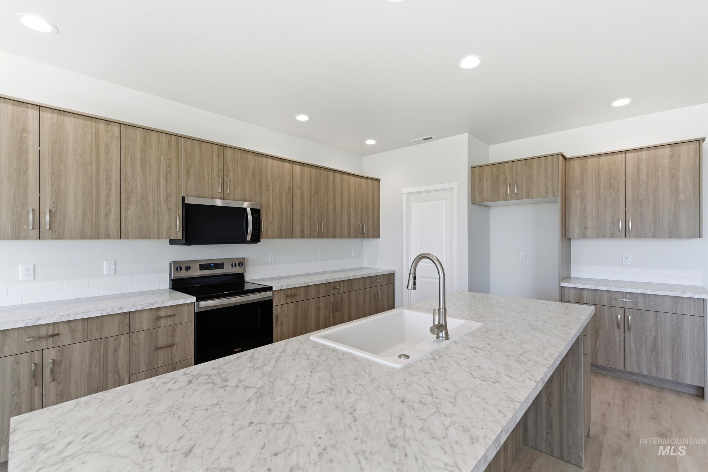 13663 Redway Court Caldwell, ID 83607 - Photo 4 of 32 Modern kitchen featuring light wood-finish cabinetry, light-toned countertops, a stainless steel microwave and range, and a large center island with an undermount sink