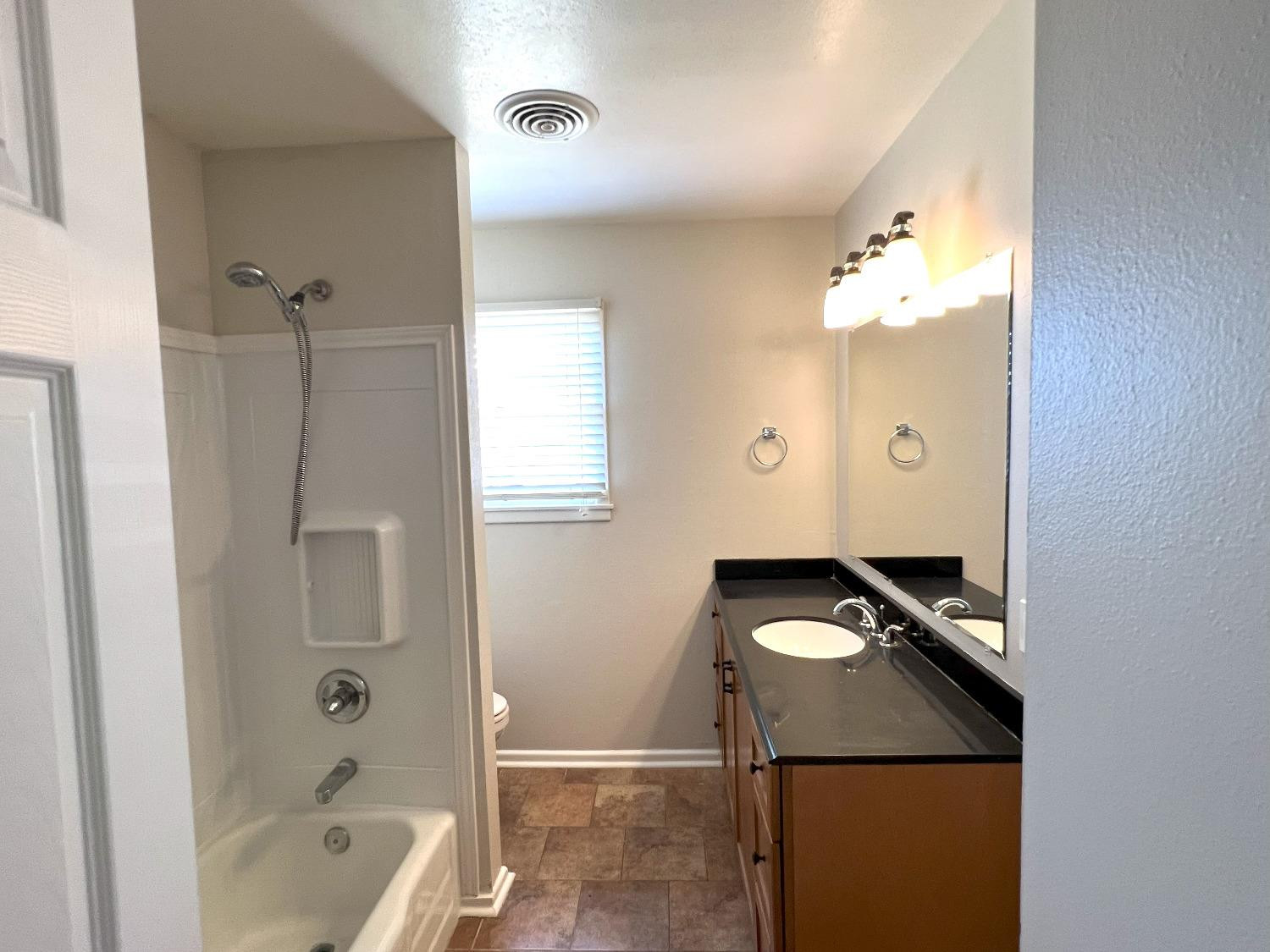4214 54th Street Lubbock, TX 79413 - Photo 6 of 18 a bathroom with a granite countertop sink a toilet and bathtub