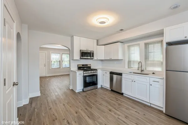 a kitchen with stainless steel appliances granite countertop a stove top oven a sink a refrigerator white cabinets and wooden floor