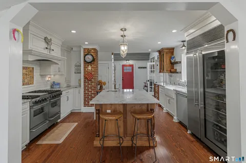 a kitchen with stainless steel appliances kitchen island granite countertop a stove a sink a refrigerator and a dining table with wooden floor