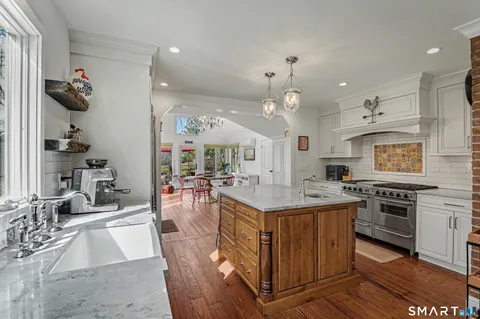 a kitchen with stainless steel appliances kitchen island granite countertop a stove top oven a sink a dining table and chairs with wooden floor