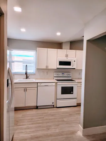 a kitchen with white cabinets a sink a stove and white stainless steel appliances