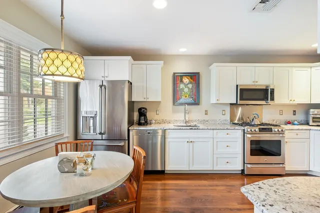 a kitchen with stainless steel appliances granite countertop a stove a sink a microwave a refrigerator and white cabinets with wooden floor