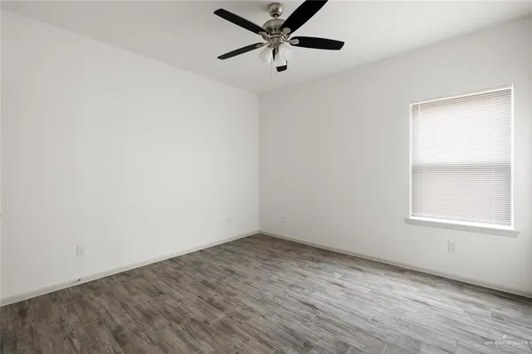an empty room with wooden floor ceiling fan and windows