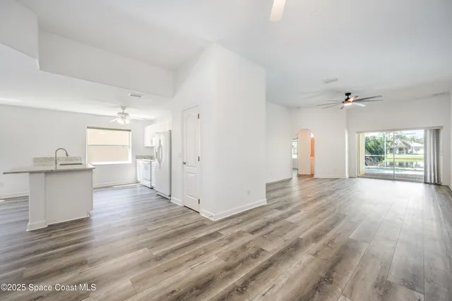 an empty room with wooden floor a ceiling fan and windows