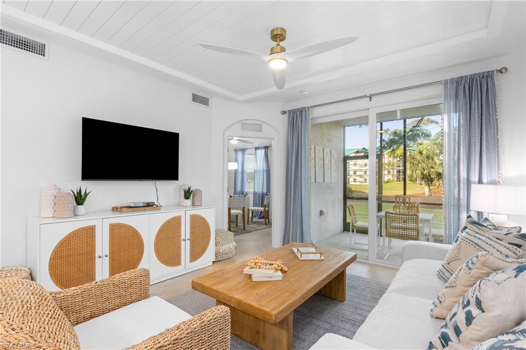 Living room with tile patterned flooring, arched walkways, a ceiling fan, wood ceiling, and a tray ceiling