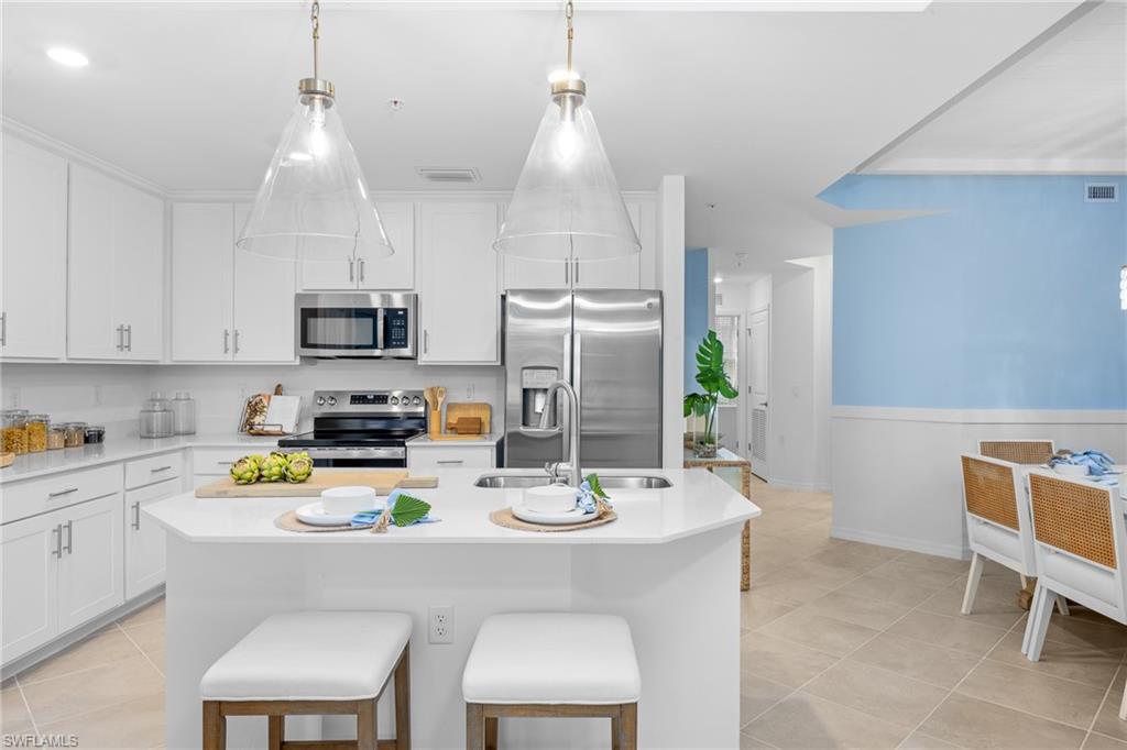 18461 Copperhead Drive, Unit 418 Lehigh Acres, FL 33936 - Photo 12 of 33 Kitchen featuring stainless steel appliances, light countertops, light tile patterned floors, white cabinetry, and an island with sink