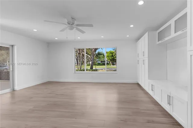 an empty room with wooden floor a ceiling fan and windows