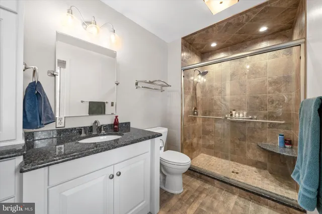 a bathroom with a granite countertop sink a toilet a mirror and shower