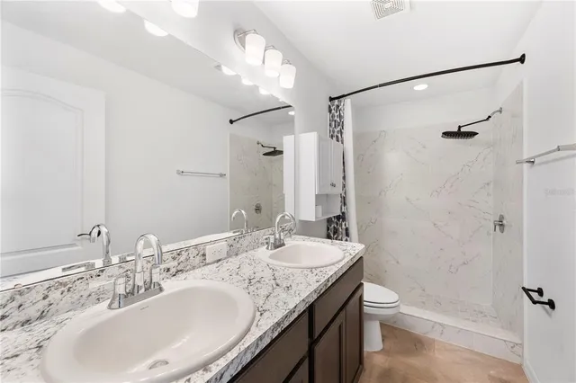 a bathroom with a granite countertop sink a toilet a mirror and shower