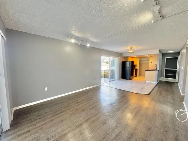 an empty room with wooden floor and kitchen view