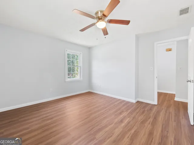 an empty room with wooden floor ceiling fan and windows