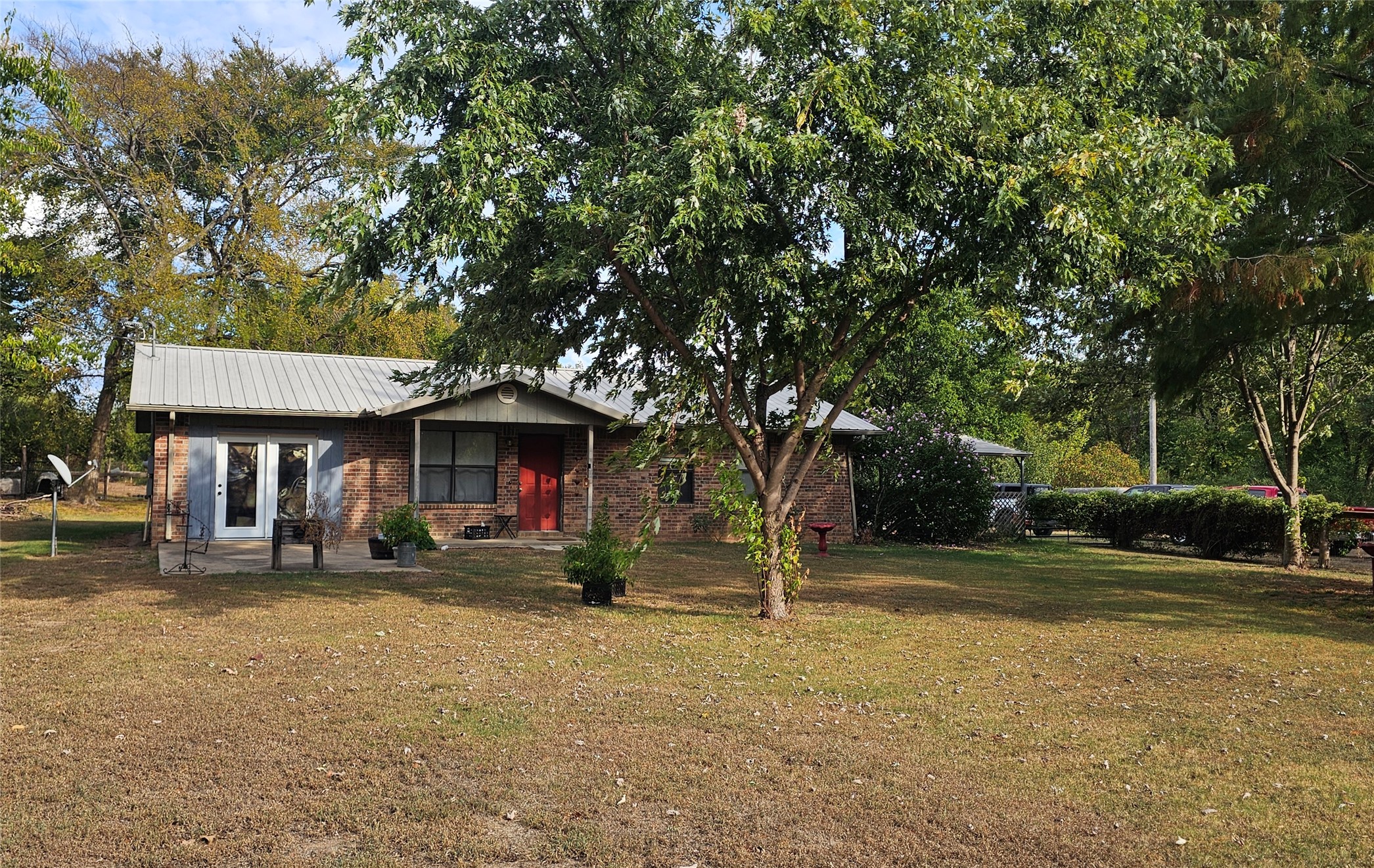 106441 South 4163rd Road Checotah, OK 74426 - Photo 14 of 17 Brick exterior with a metal roof, featuring a covered entryway with a red door and a concrete patio with double French doors