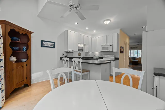 a kitchen with stainless steel appliances kitchen island granite countertop a refrigerator a stove a sink a dining table and chairs with wooden floor
