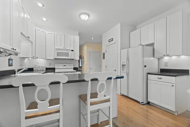 a kitchen with stainless steel appliances granite countertop a refrigerator a stove a sink and white cabinets with wooden floor