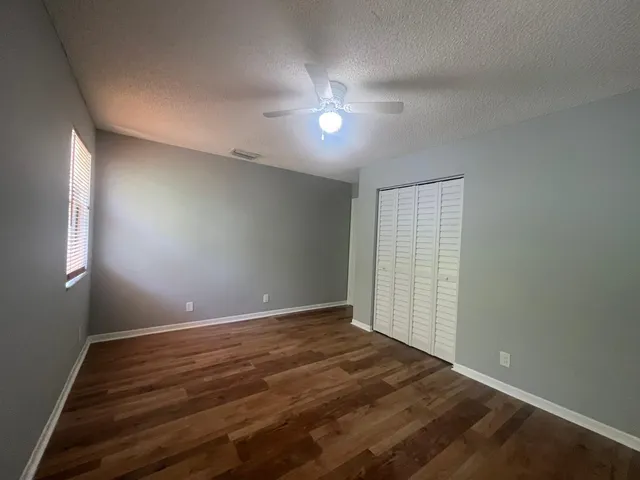 an empty room with wooden floor fan and windows