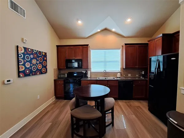 a kitchen with granite countertop a refrigerator a stove a sink a dining table and chairs with wooden floor