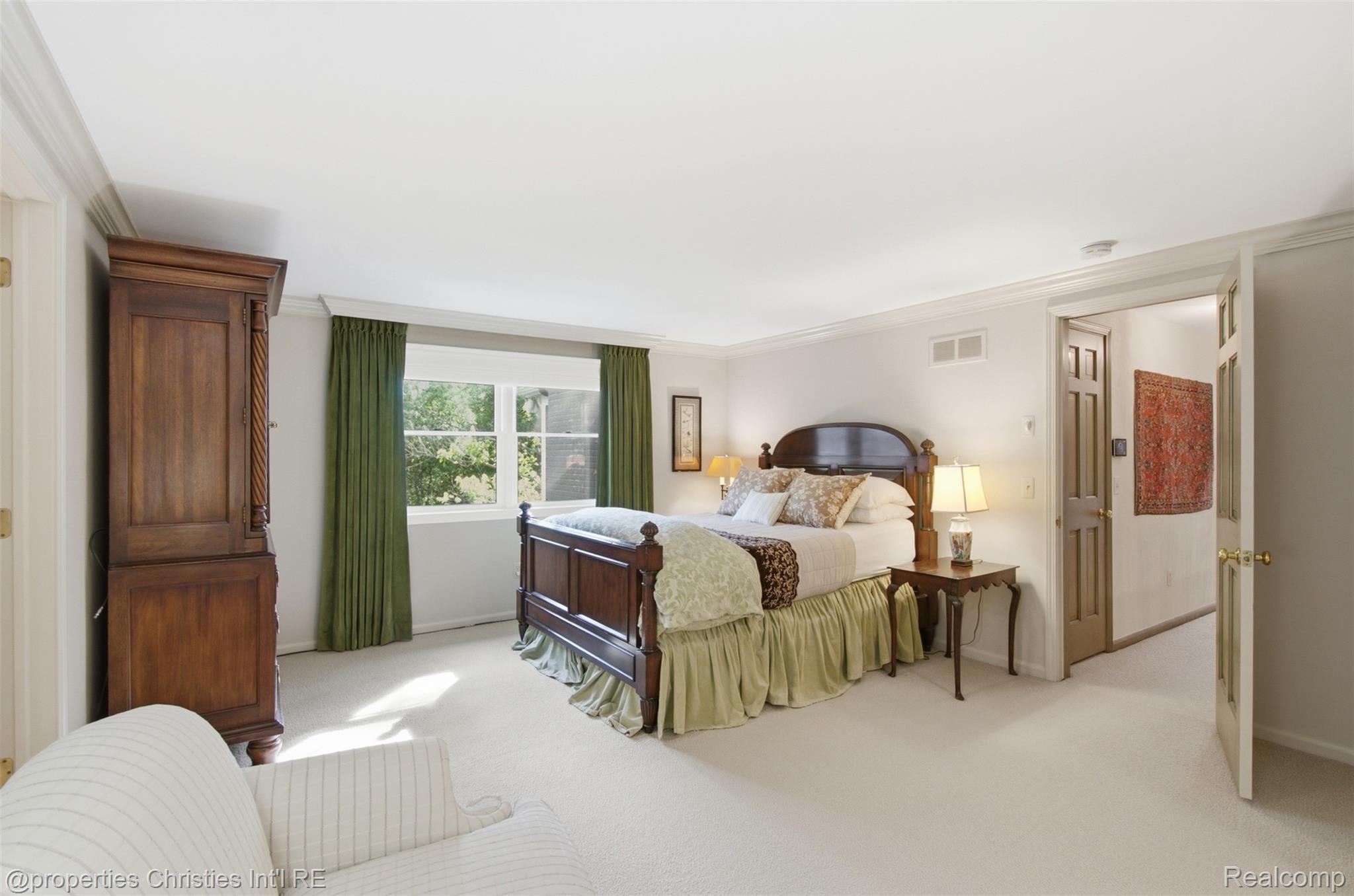 25235 Canterbury Road Franklin, MI 48025 - Photo 26 of 56 Spacious primary bedroom featuring broadloom carpeting, a large window with privacy treatments, crown molding, and a paneled door