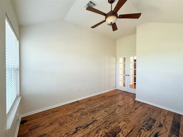 an empty room with wooden floor fan and windows