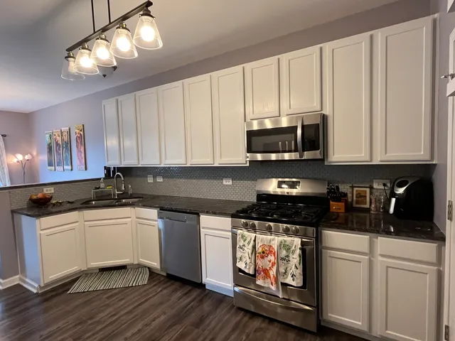 a kitchen with stainless steel appliances granite countertop a stove a sink and white cabinets