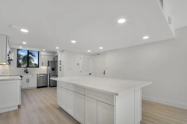 a large white kitchen with a large window a refrigerator and white cabinets
