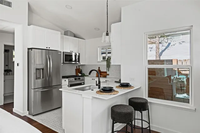 a kitchen with stainless steel appliances a refrigerator a stove a sink dishwasher a dining table and chairs with wooden floor