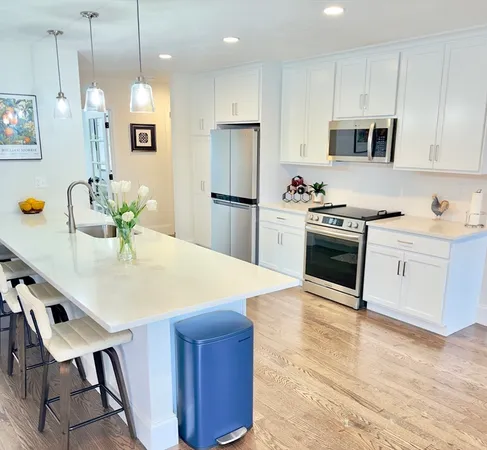 a kitchen with stainless steel appliances kitchen island granite countertop a stove a sink a microwave a refrigerator and white cabinets with wooden floor